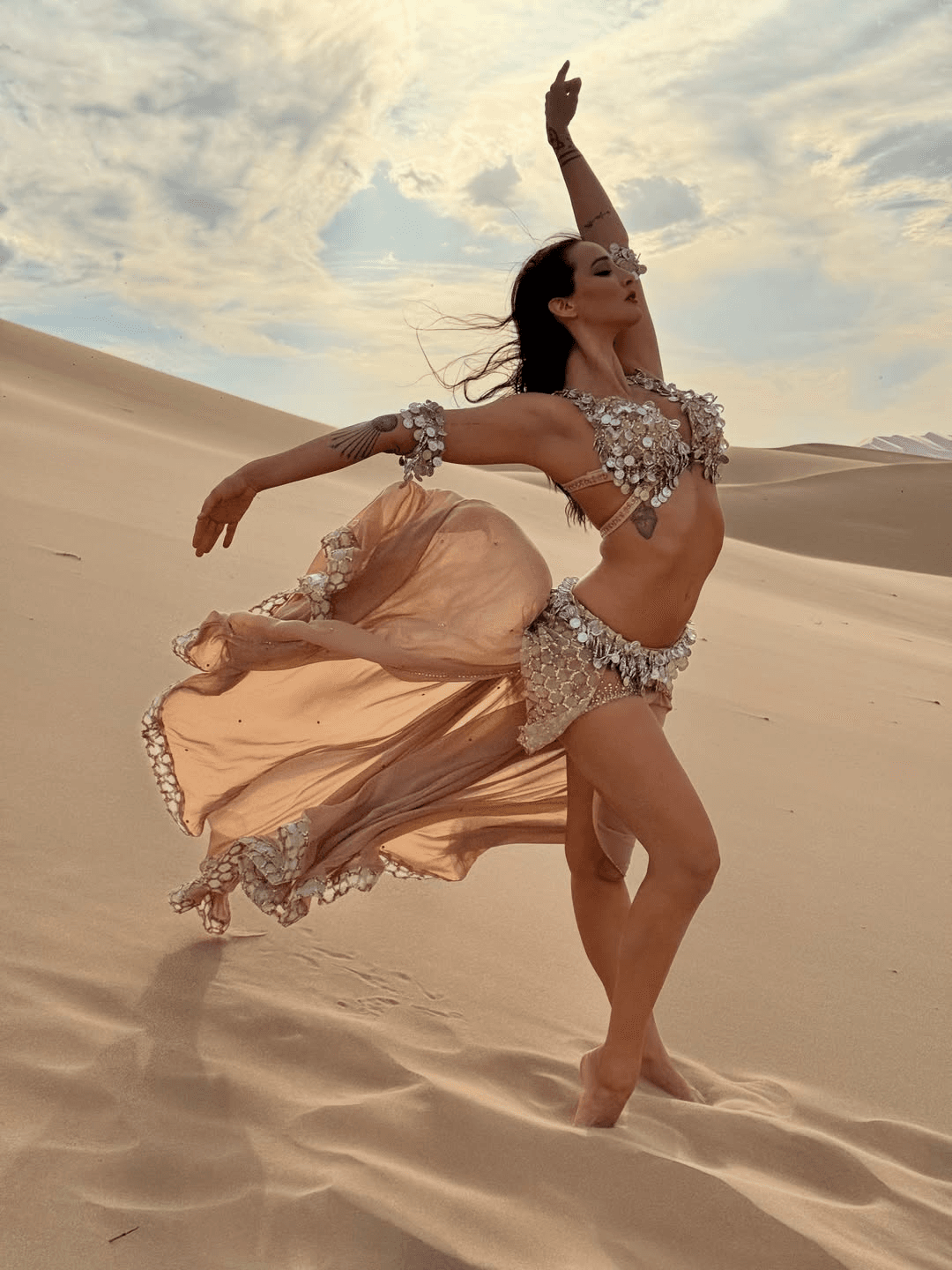 Dancer on a desert dune in a champagne costume, the veil skirt flowing with her movement