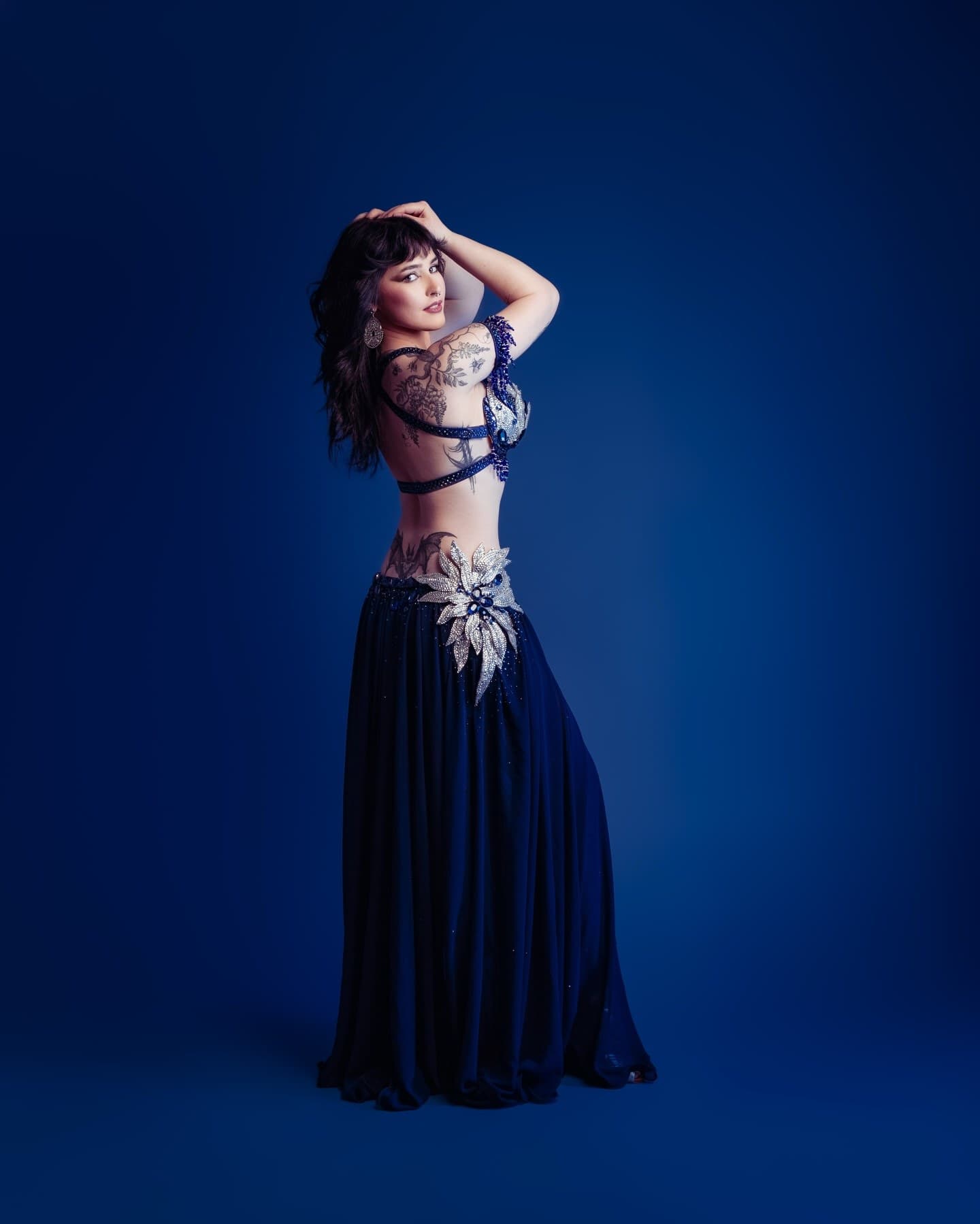 Maja Amani in a blue and silver costume with a white veil, posing against a blue backdrop